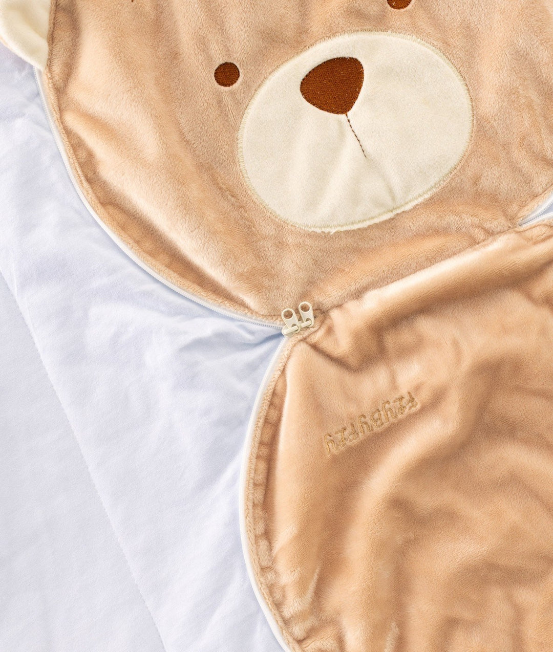Close-up of silver zipper pull connecting plush bear head to blanket body