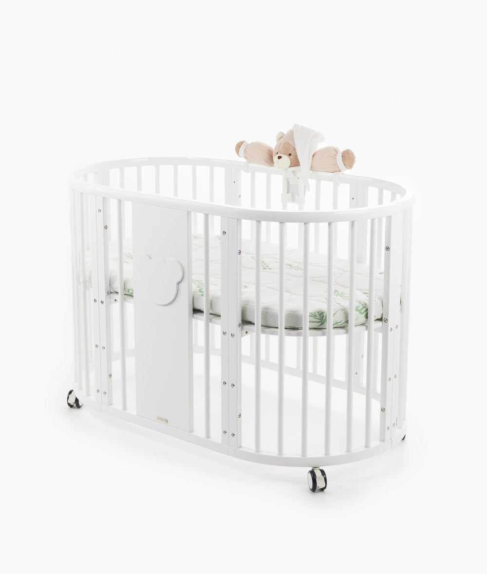 White baby cot with teddy bear design styled in a neutral nursery room