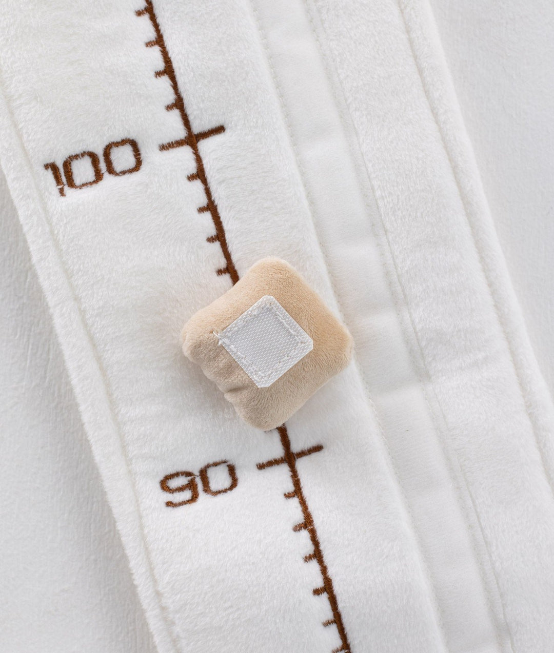 Macro view of white绒 fabric growth chart showing embroidered numbers and square beige velcro marker