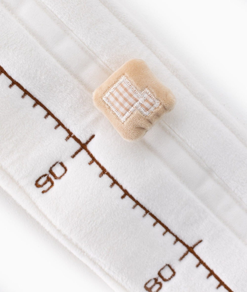 Detail shot of growth chart scale with embroidered numbers and square beige marker featuring gingham bow