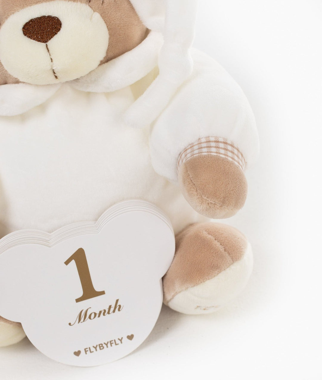 Close up of white cloud-shaped 1 Month milestone card against soft beige bear texture