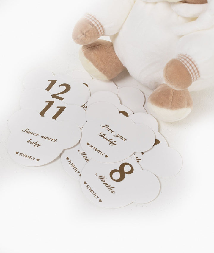 Scattered set of white cloud milestone cards with brown text next to beige bear