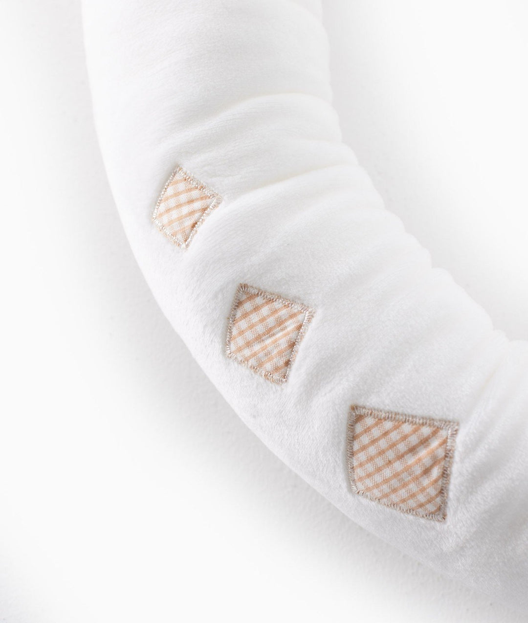 Close-up of beige gingham diamond patches on white baby bolster fabric