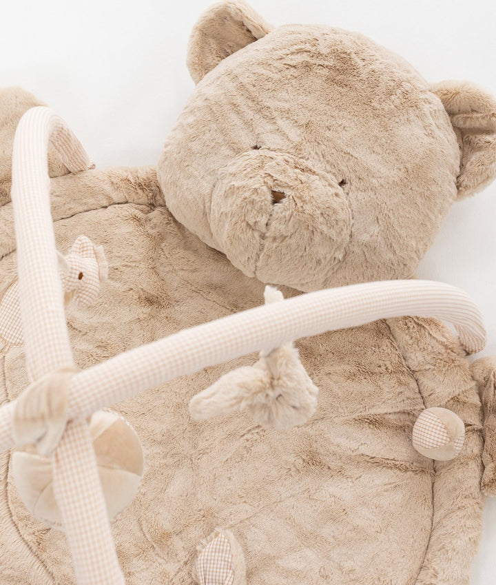 Top down view of soft beige bear head pillow and gingham covered arch bars on padded playmat surface