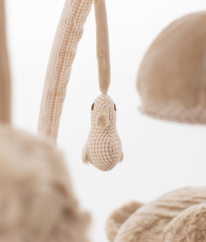 Detail shot of beige and white gingham check bird toy hanging from arch bar against blurred background