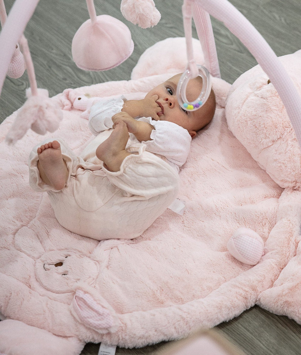 Baby lying on pink bear playmat reaching for hanging rattle ring demonstrating use case