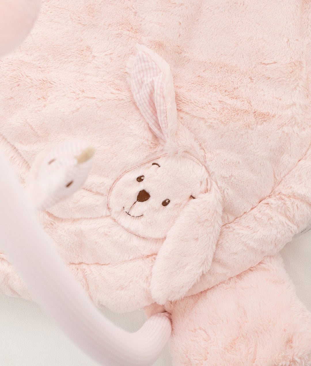 Macro shot of dense plush pink playmat texture with embroidered bunny face and gingham ears