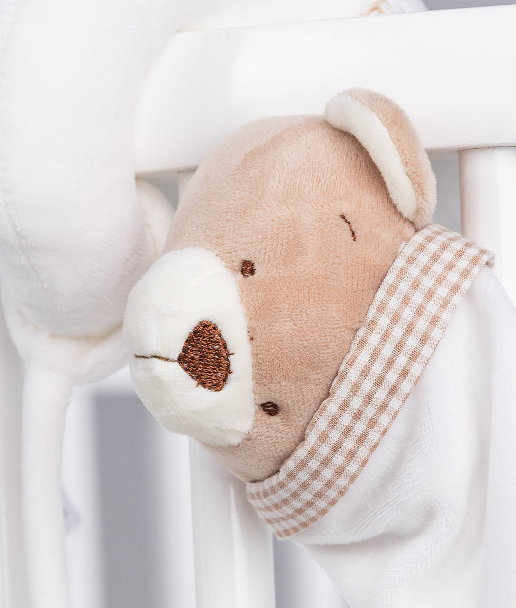 Close up of beige plush bear face on spiral toy with brown gingham scarf