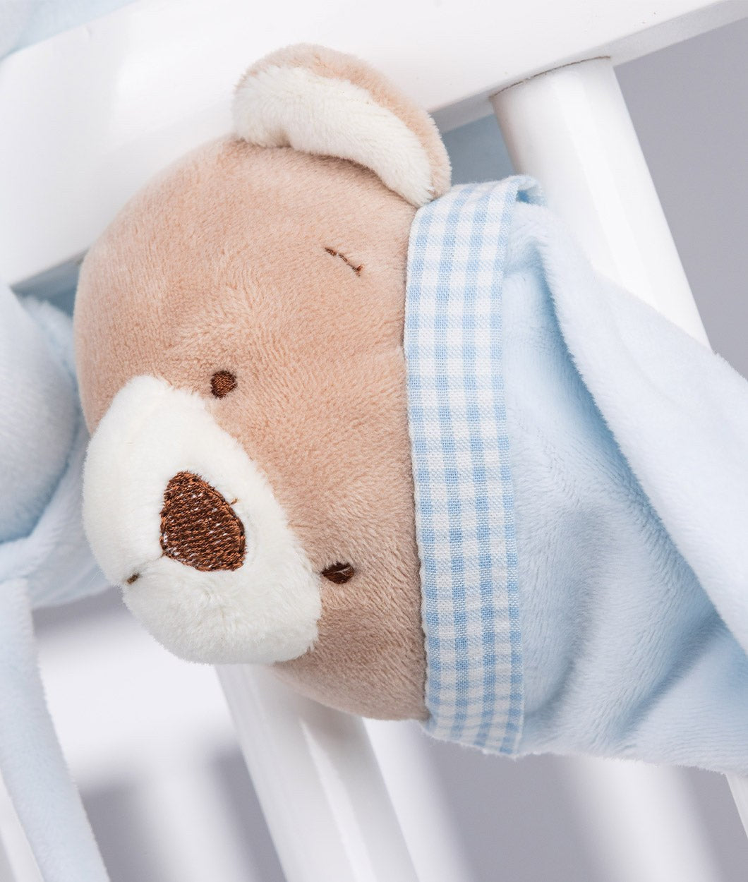 Close-up of tan plush bear face with embroidered nose and blue gingham fabric band