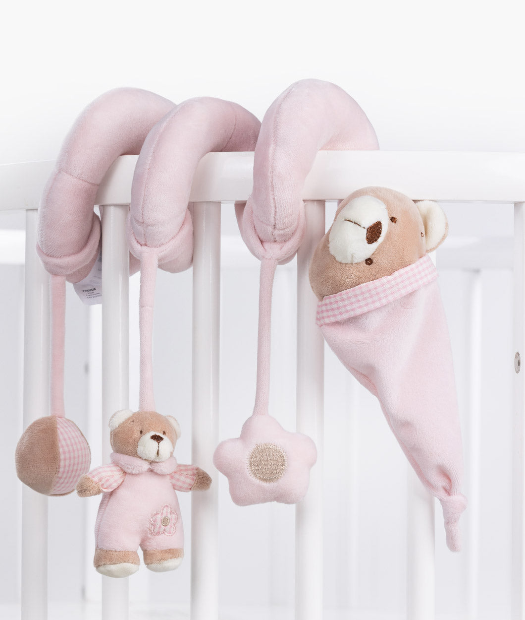Pink spiral activity toy draped over white cot rail with hanging bear, star, and checkered ball charms