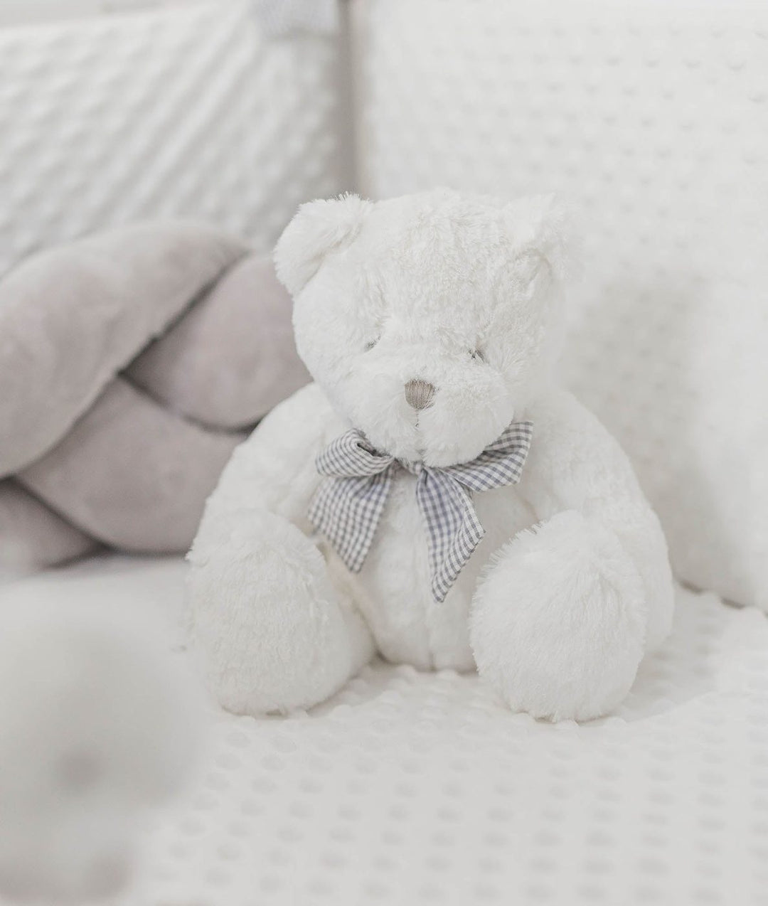 fluffy white teddy bear in grey checkered bow tie on dotted bedding
