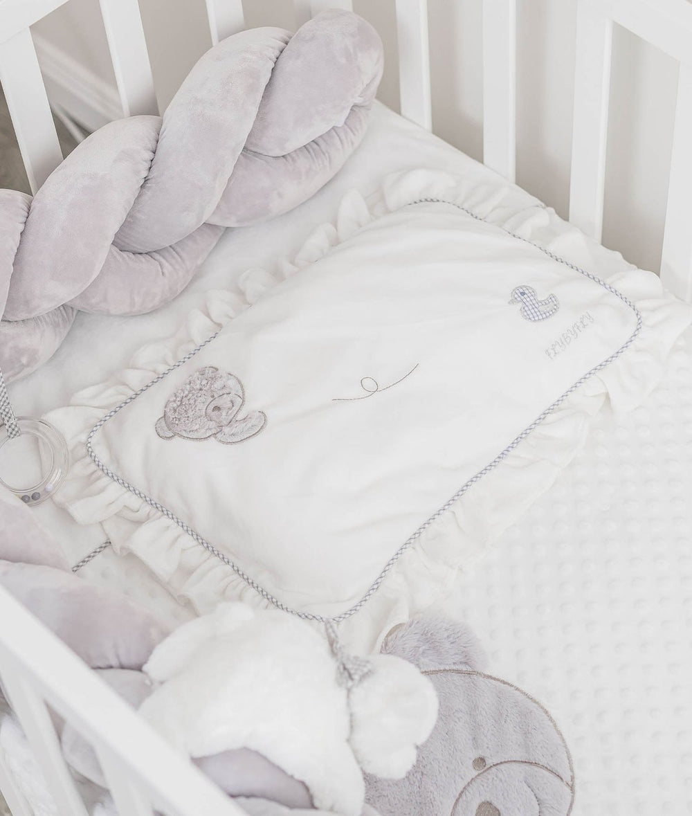 ruffled pillow with grey trim and embroidered details next to grey bumper