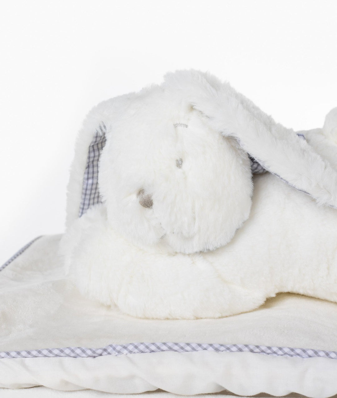 Side view of white plush bunny on cream fabric lid with grey gingham piping trim on wicker basket