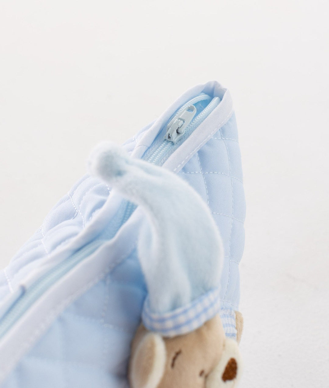 Close-up of silver zipper pull, white piping, and soft plush bear hat texture on blue bag