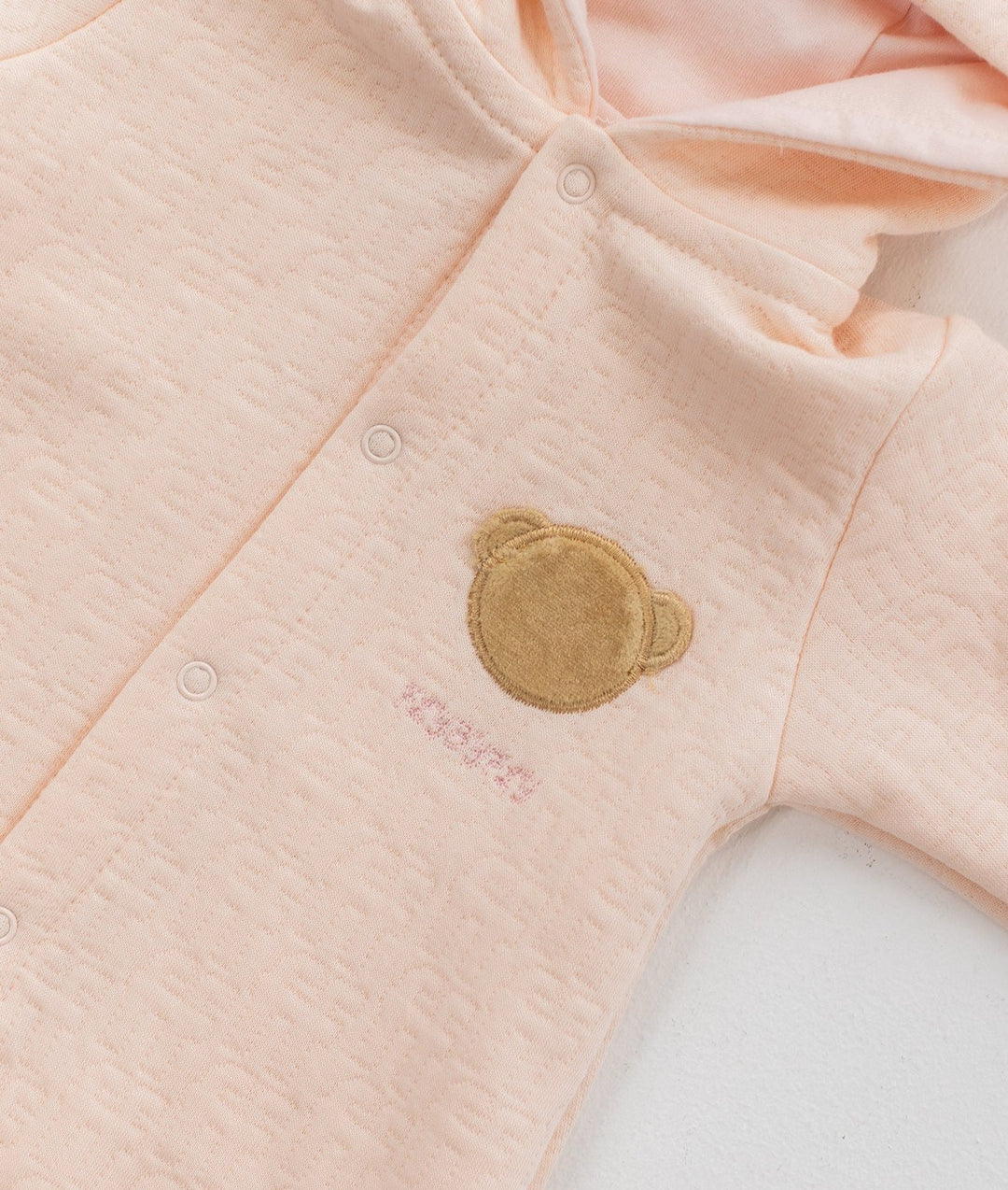 Light pink waffle cotton baby jumpsuit with embroidered bear face patch detail
