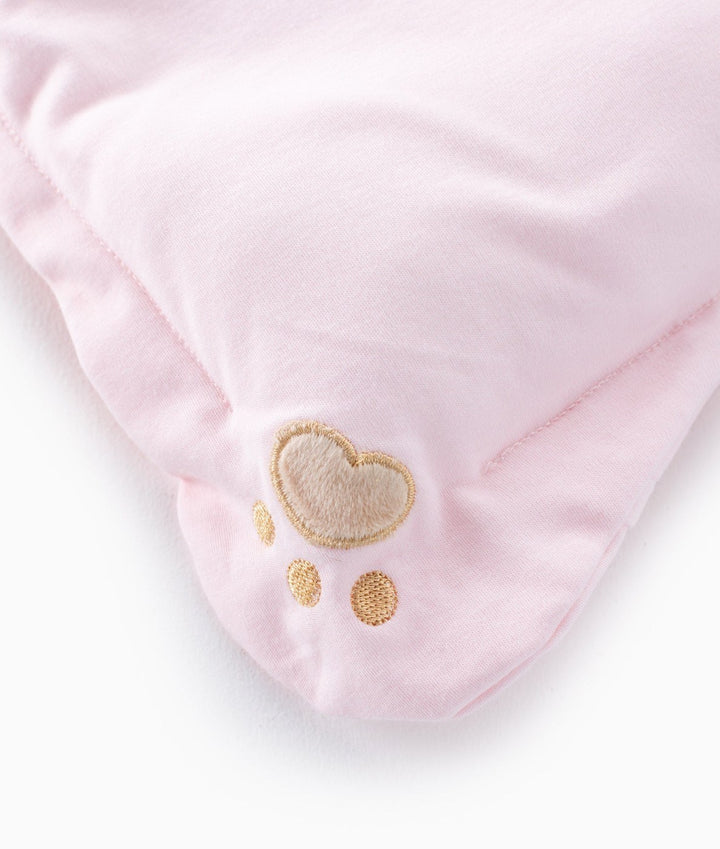 Close-up pink cotton pillow corner showing embroidered beige paw print with gold stitched toe accents