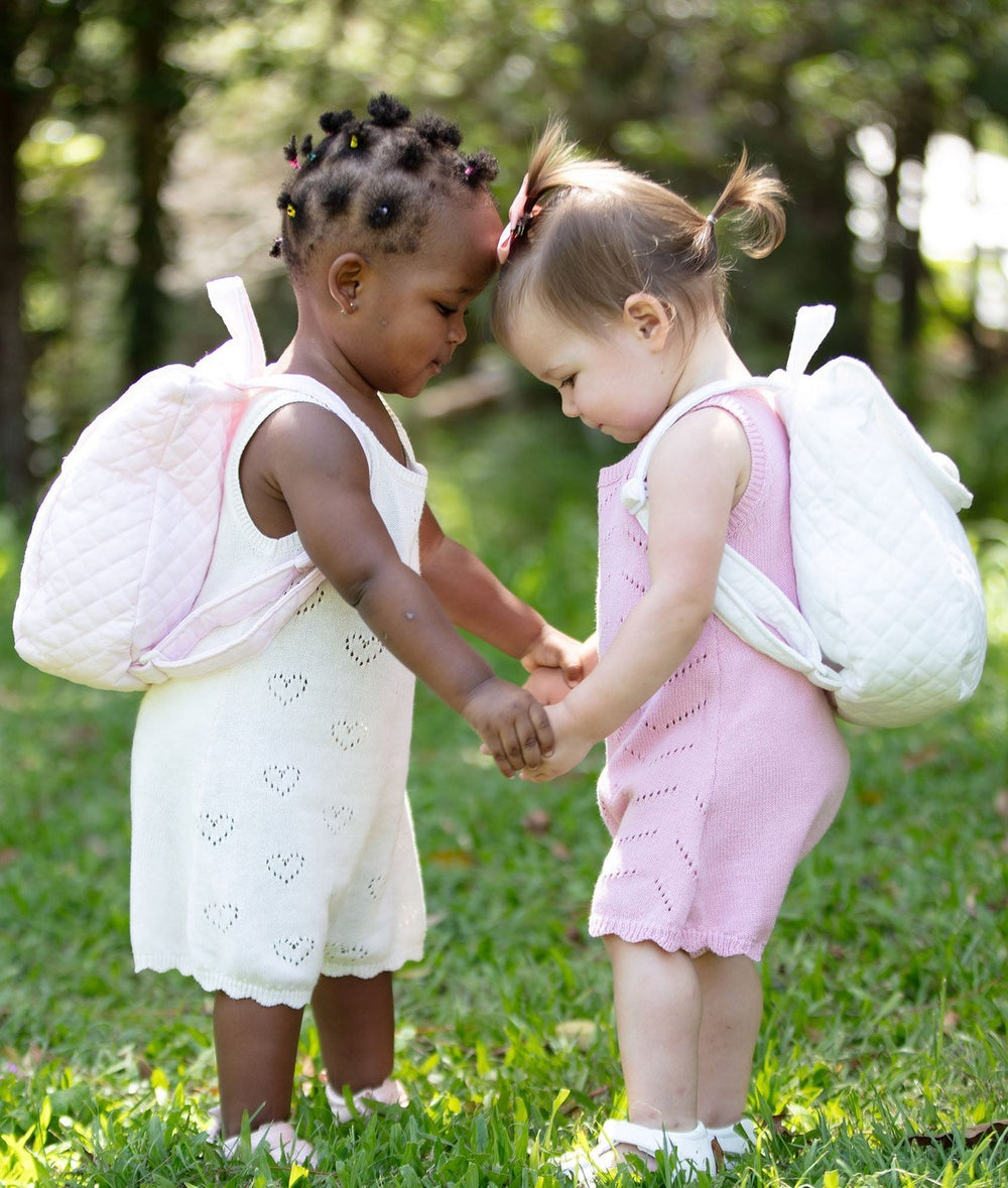 Toddlers wearing pink and white quilted backpacks in outdoor setting