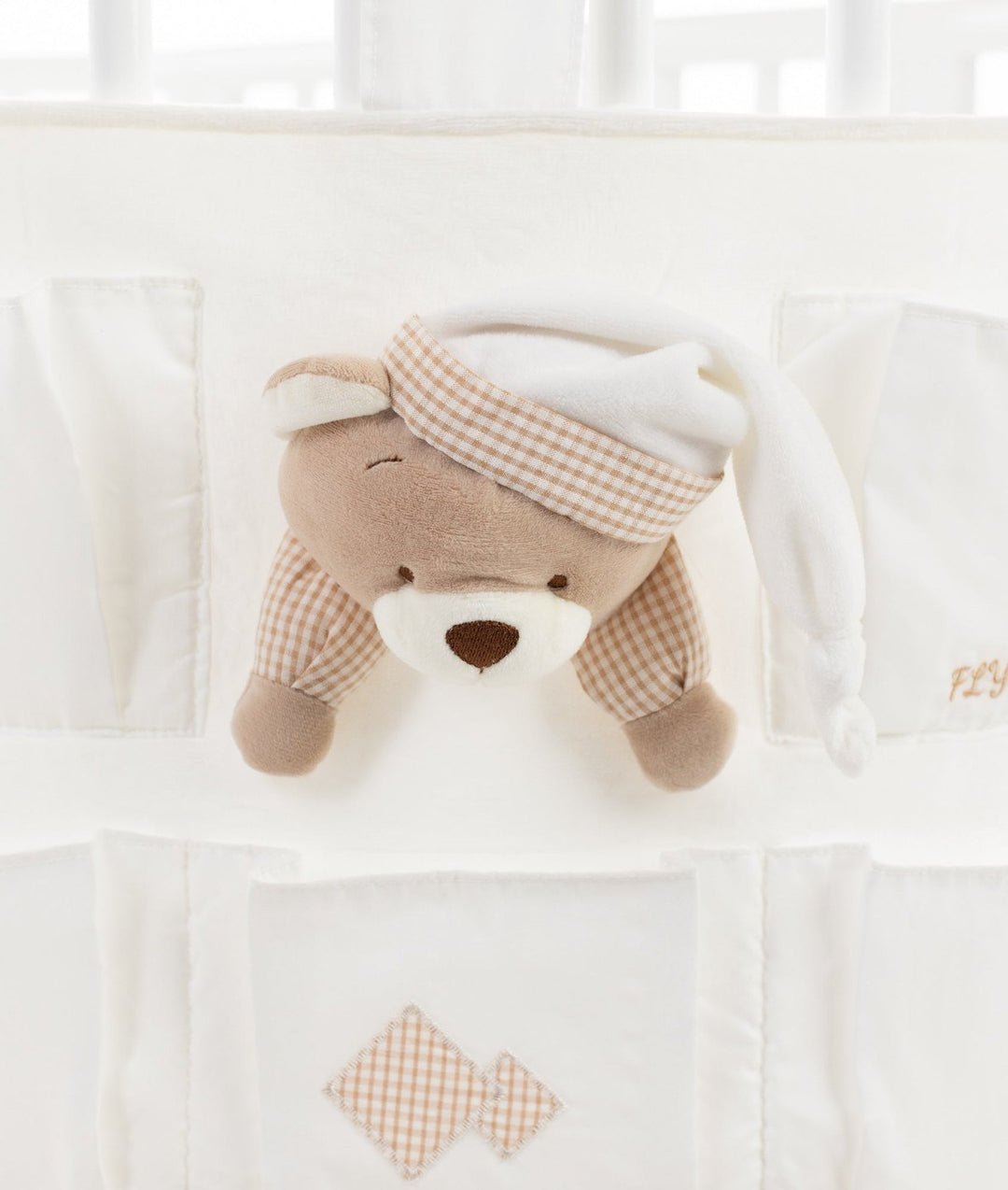 Macro detail of brown plush teddy bear face with closed eye and beige gingham sleep cap integrated into white fabric organiser