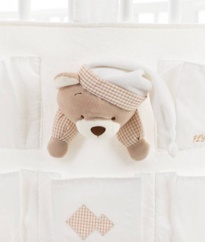 Macro detail of brown plush teddy bear face with closed eye and beige gingham sleep cap integrated into white fabric organiser