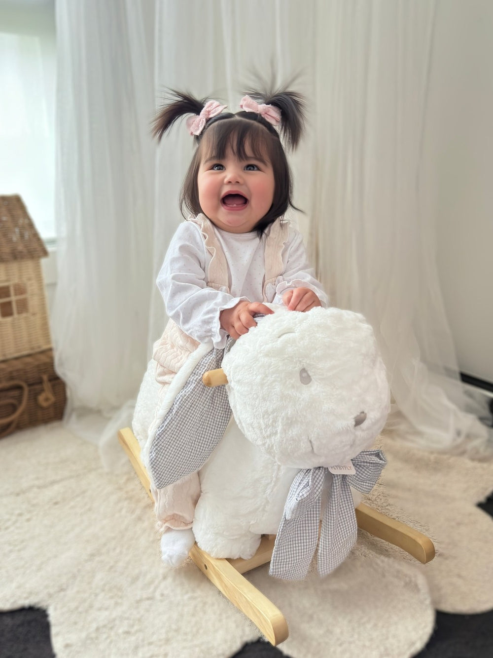 Toddler girl sitting on grey and white rocking bunny holding wooden handle for balance play