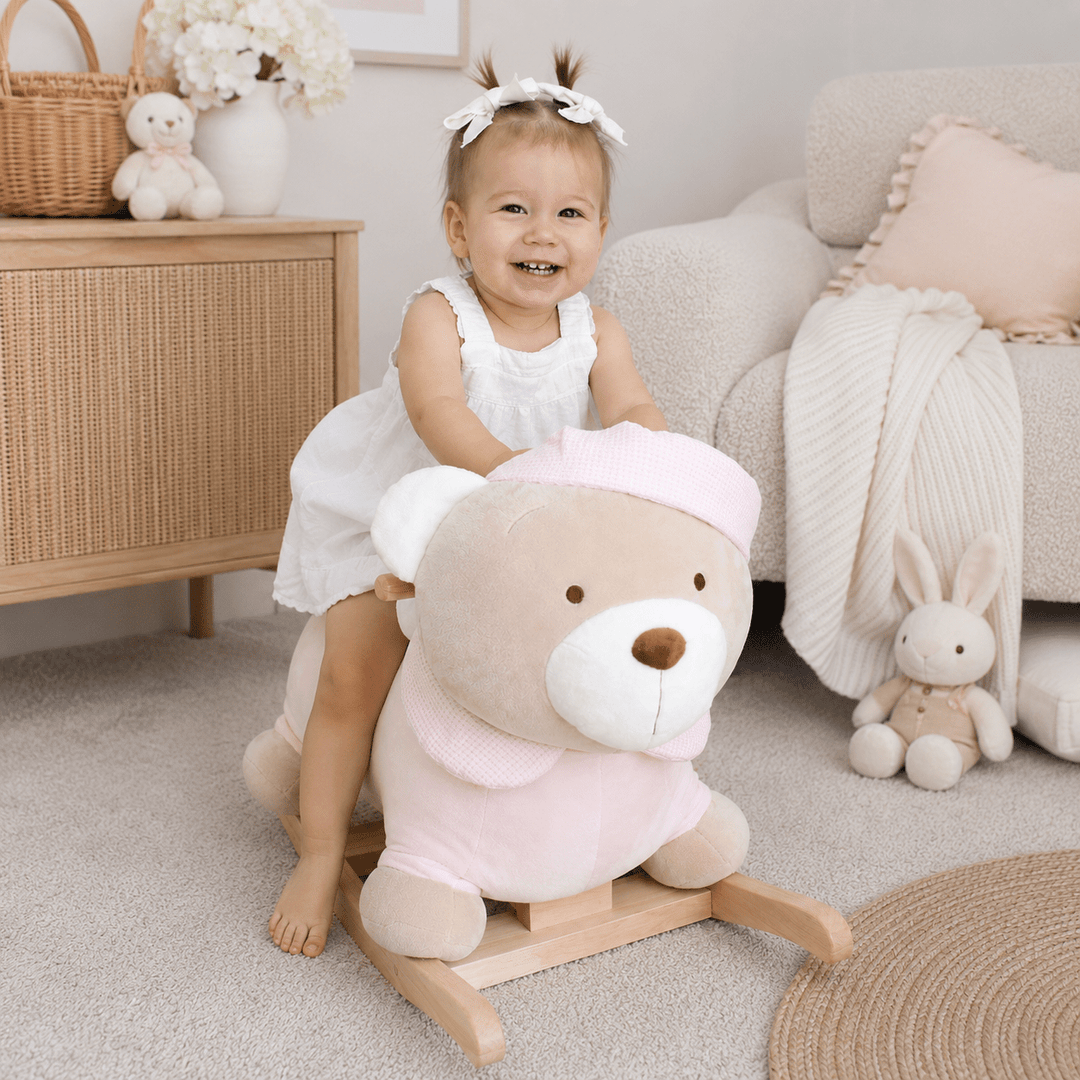 Toddler sitting on pink rocking teddy bear in nursery