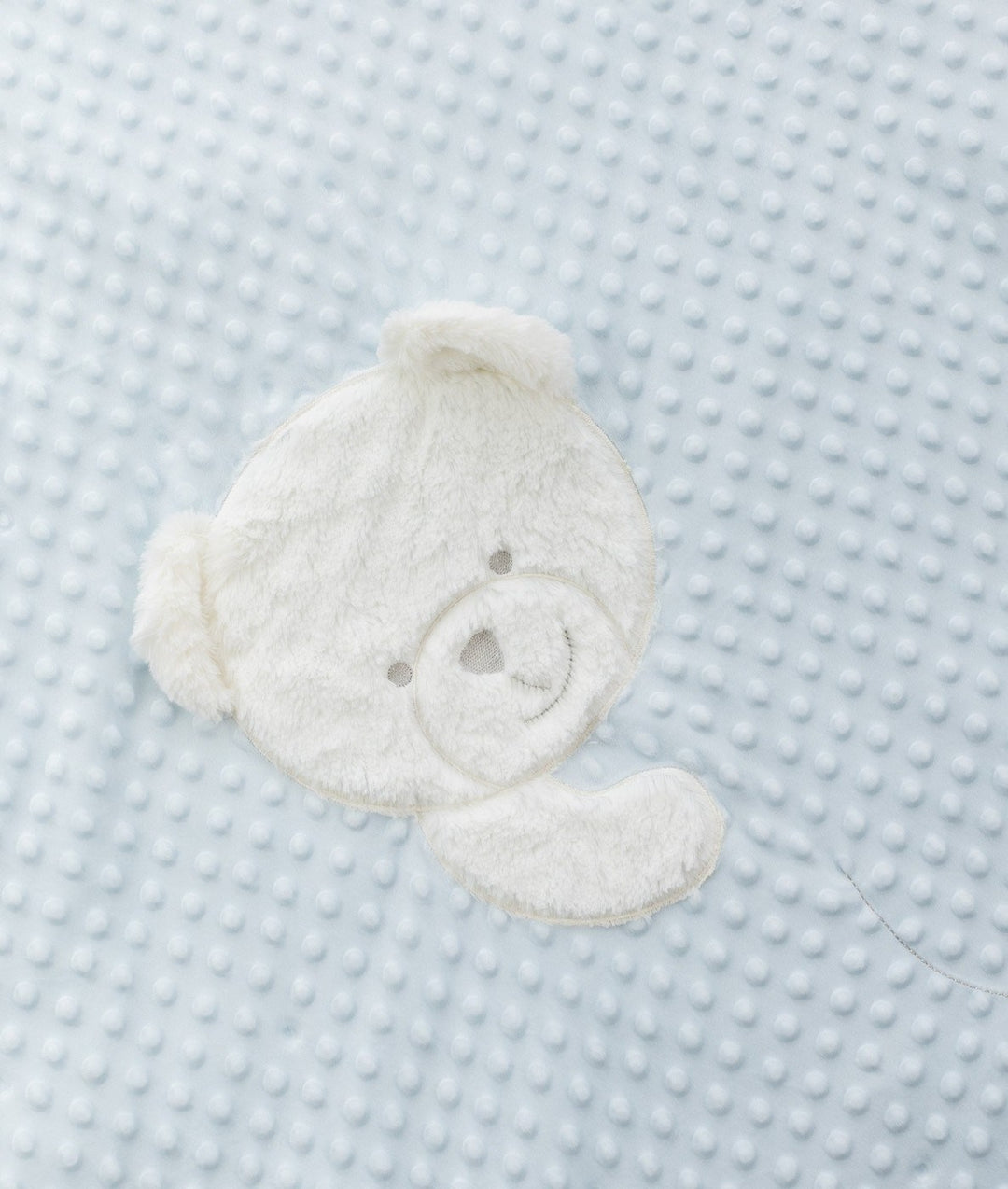 Macro view of white plush teddy bear face patch on light blue dotted minky fabric
